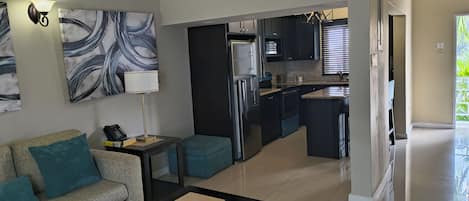 A modern living room with a sofa, a coffee table, and a kitchen area with dark cabinets and stainless steel appliances.