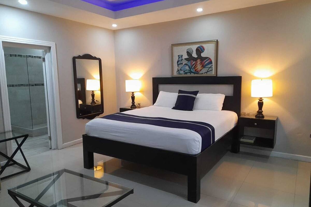 Une chambre d’hôtel moderne avec un grand lit, des lampes de chevet, une table basse en verre, un miroir et un tableau au mur.