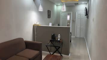 Una sala de estar con un sofá, una mesa de centro de madera y una mesita auxiliar con un teléfono y una botella.