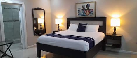 A modern hotel room with a large bed, bedside lamps, a glass coffee table, a mirror, and a painting on the wall.