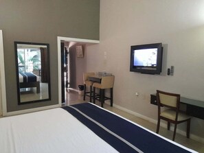 Quarto de hotel com cama, escrivaninha, cadeira, televisão e espelho.