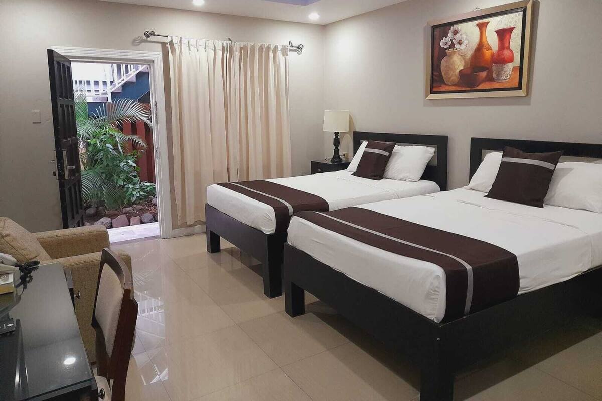 Une chambre d’hôtel avec deux lits, un bureau, une chaise, un tableau et une vue sur l’extérieur.