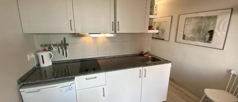 Een kleine keuken met witte kastjes, een inbouwoven en een spoelbak.