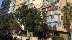 A multi-story residential building with balconies, a stone facade, and a clear sky.