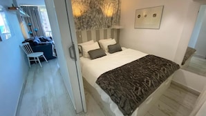 A modern bedroom with a large bed, a desk, and a chair in a separate area.