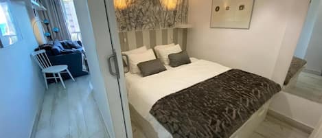 A modern bedroom with a large bed, a desk, and a chair in a separate area.