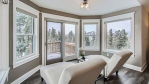 Ein Eckzimmer mit großen Fenstern, einer Deckenleuchte und Blick auf schneebedeckte Bäume.