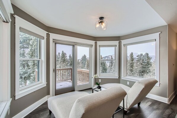 A corner room with large windows, a ceiling light, and a view of snow-covered trees.