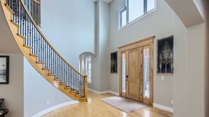 Ein geräumiger Innenraum mit einer Holztreppe, einer großen Holztür und zwei gerahmten Bildern an den Wänden.