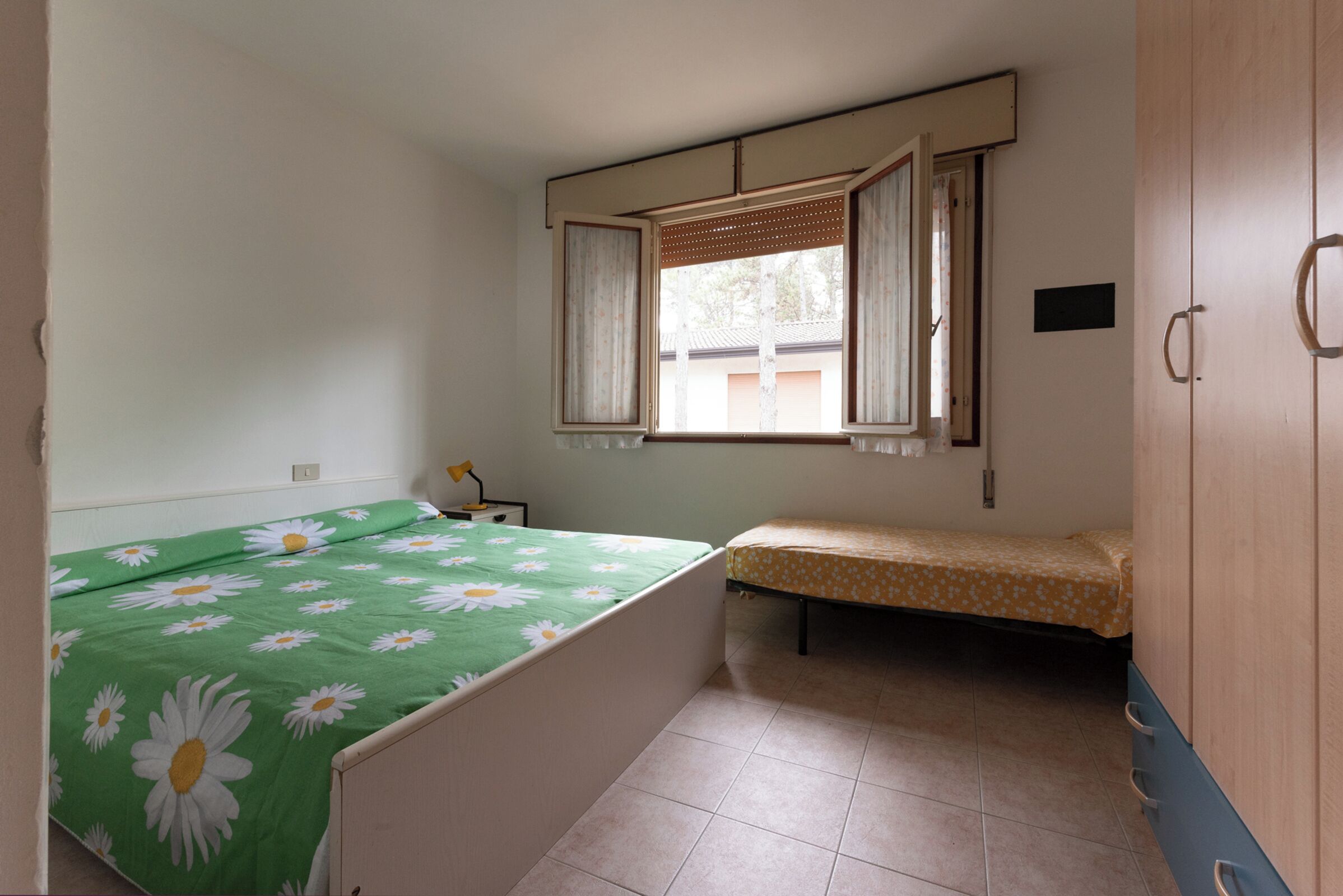 A bedroom with a single bed, a window with curtains, a bedside table, and a wardrobe.