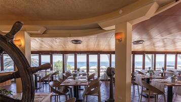 Een restaurant met uitzicht op zee, een houten plafond en gedekte tafels.