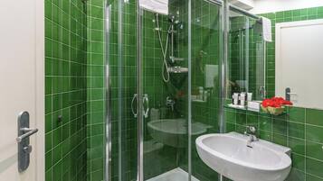 A bathroom with green tiles, a glass shower enclosure, a white sink, and a towel rack.