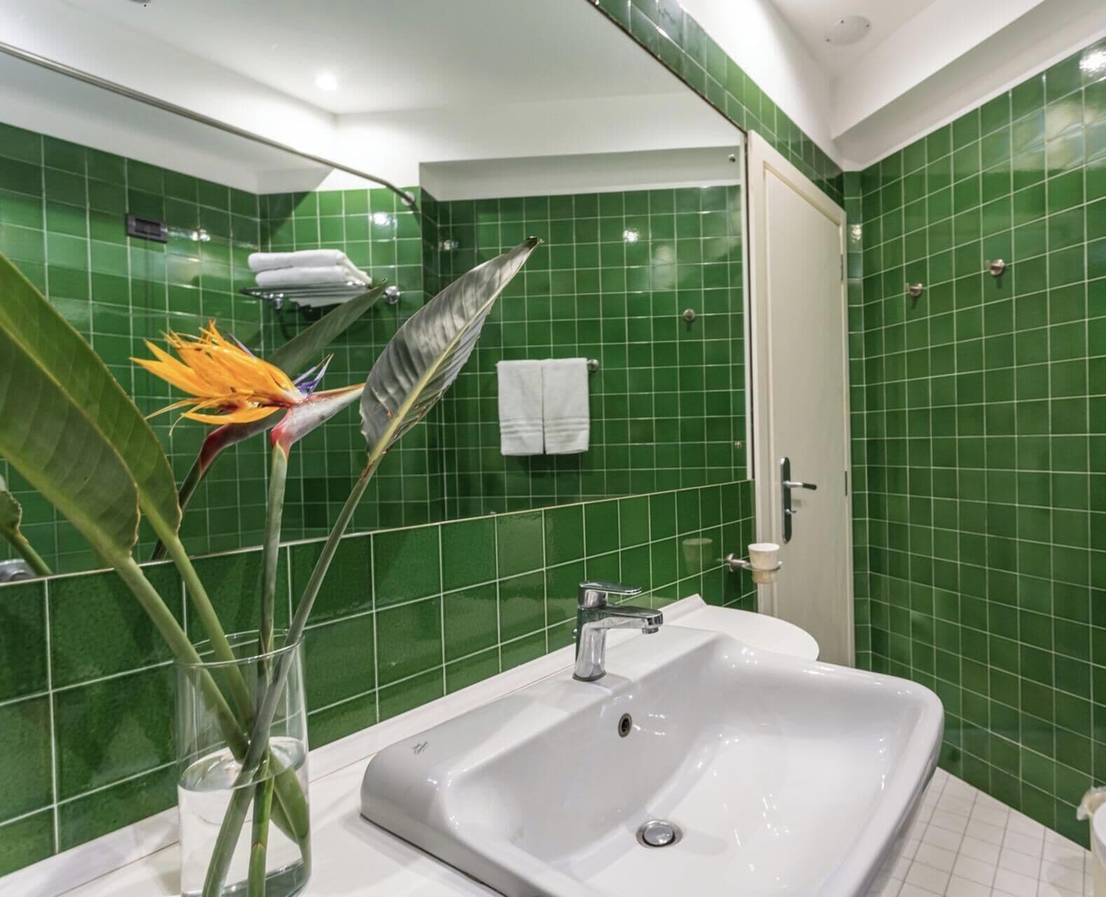 Une salle de bain avec des murs recouverts de carreaux verts, un lavabo blanc et un espace douche.