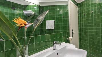 Une salle de bain avec des murs recouverts de carreaux verts, un lavabo blanc et un espace douche.