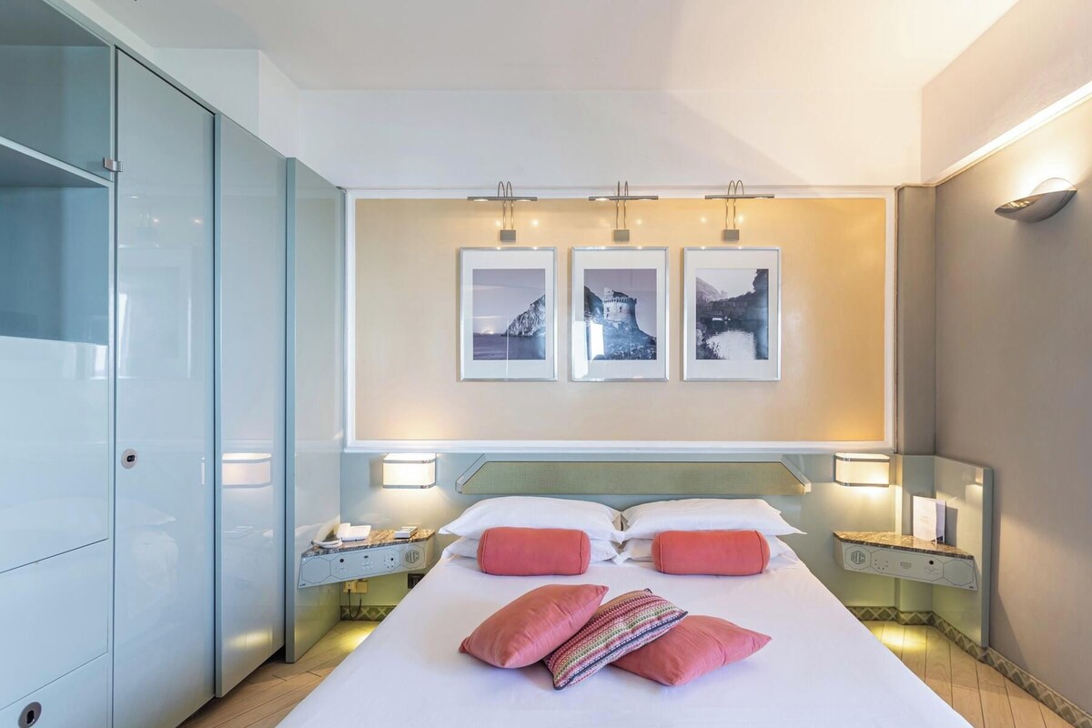 A hotel room with a large bed, bedside tables, a wardrobe, and three framed pictures on the wall.