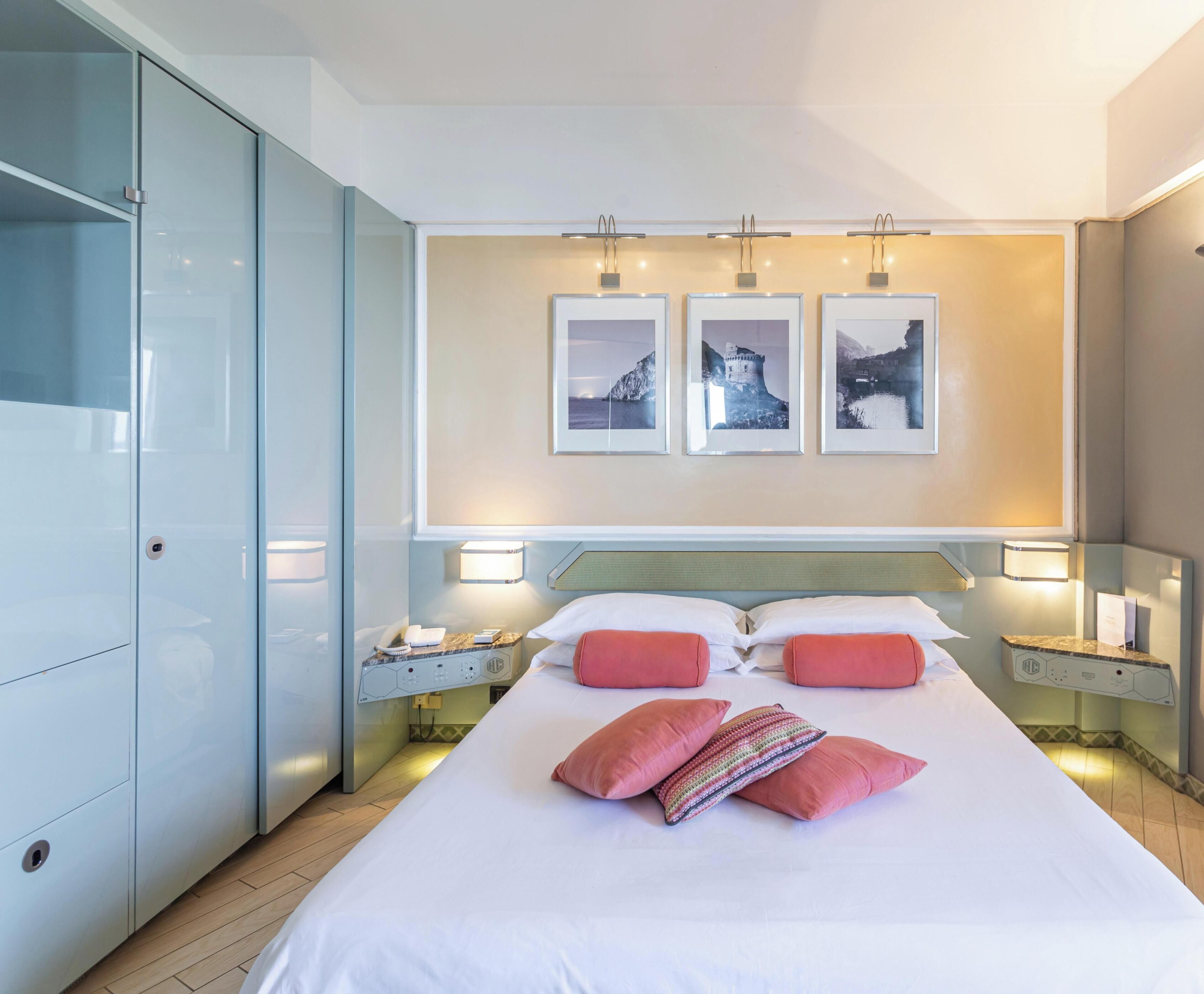 Ein Hotelzimmer mit einem großen Bett, zwei Nachttischen, einem Kleiderschrank und drei gerahmten Bildern an der Wand.