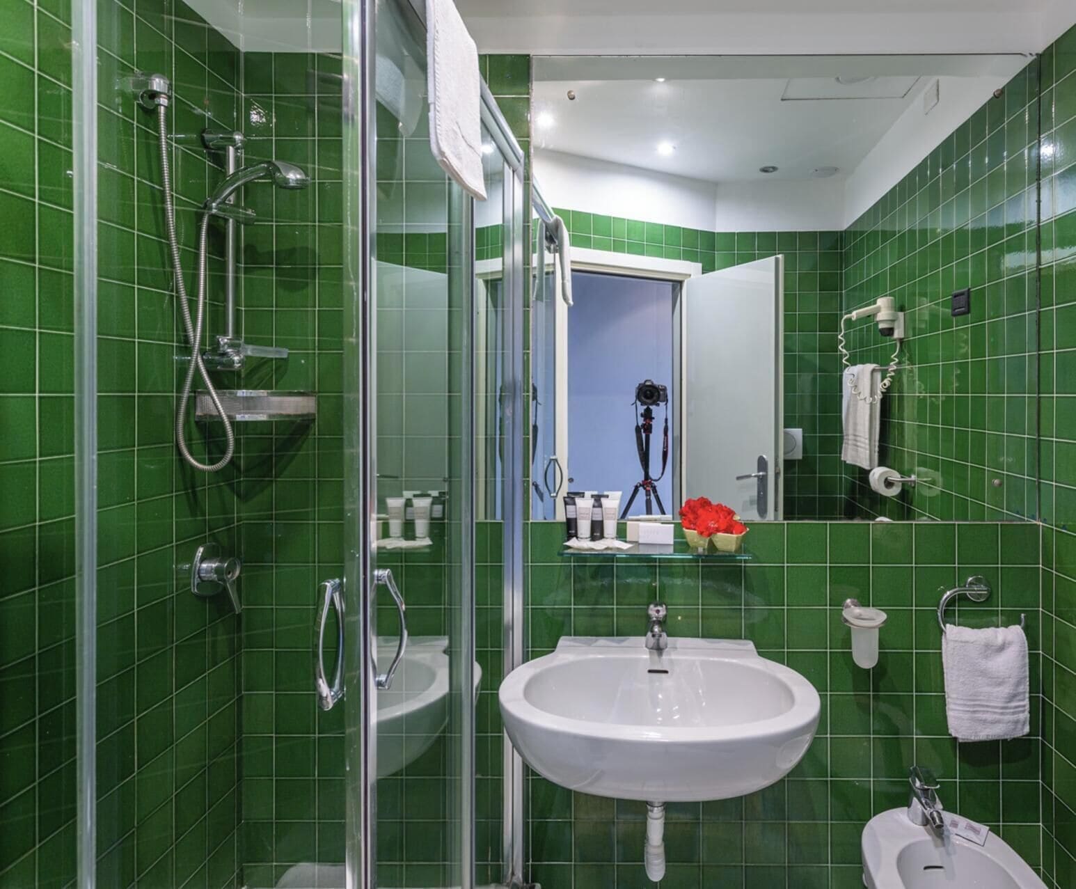 Een badkamer met groene tegels, een wastafel, een spiegel en een douche.