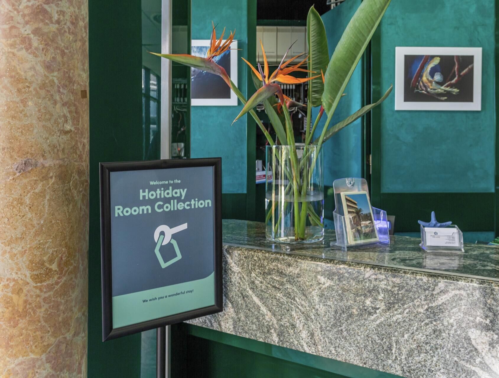 A reception desk with a framed welcome sign, a glass vase with a plant, and a framed picture on the wall.