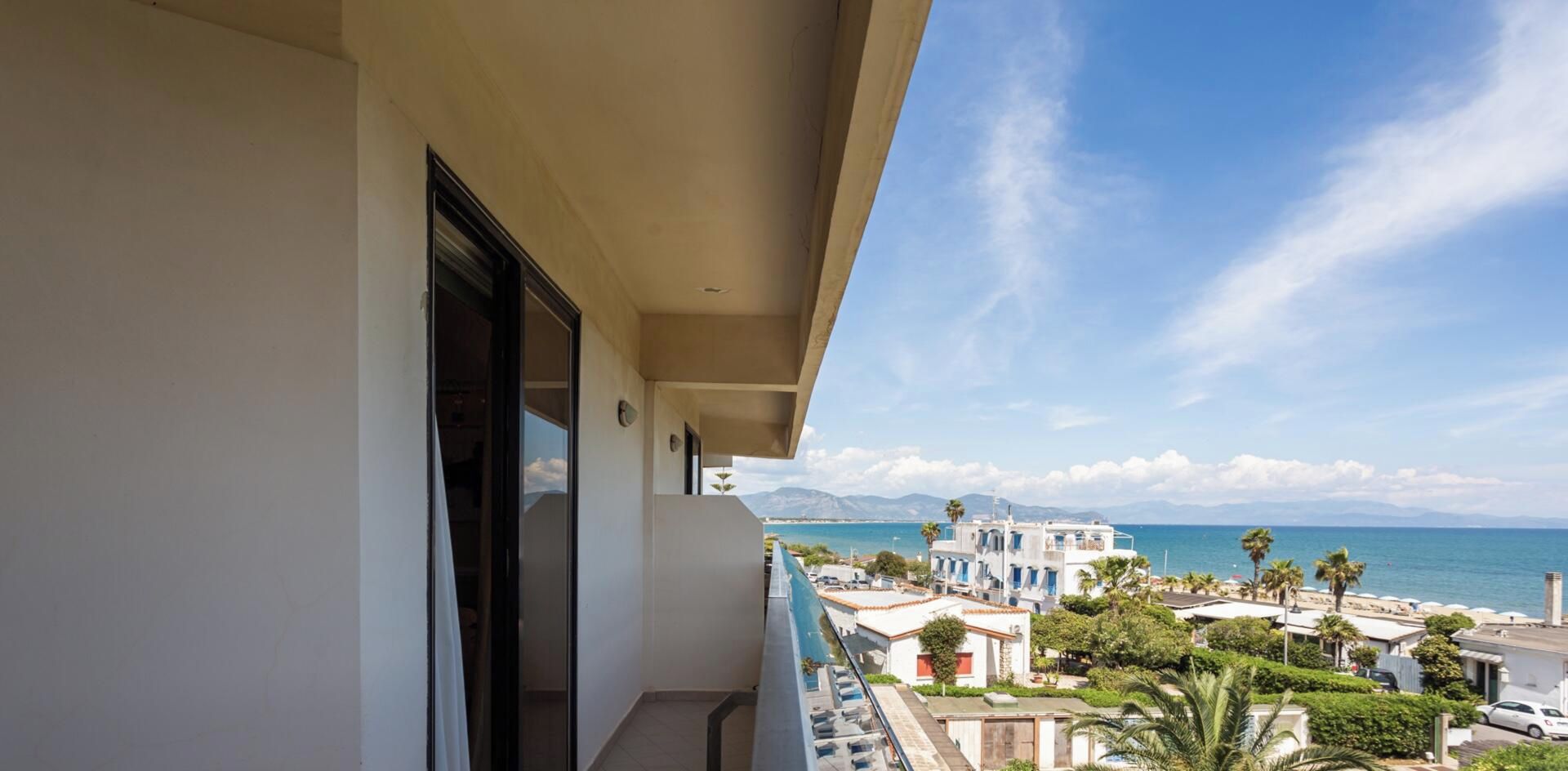 Un balcon donnant sur une ville côtière, avec vue sur les bâtiments et les palmiers.