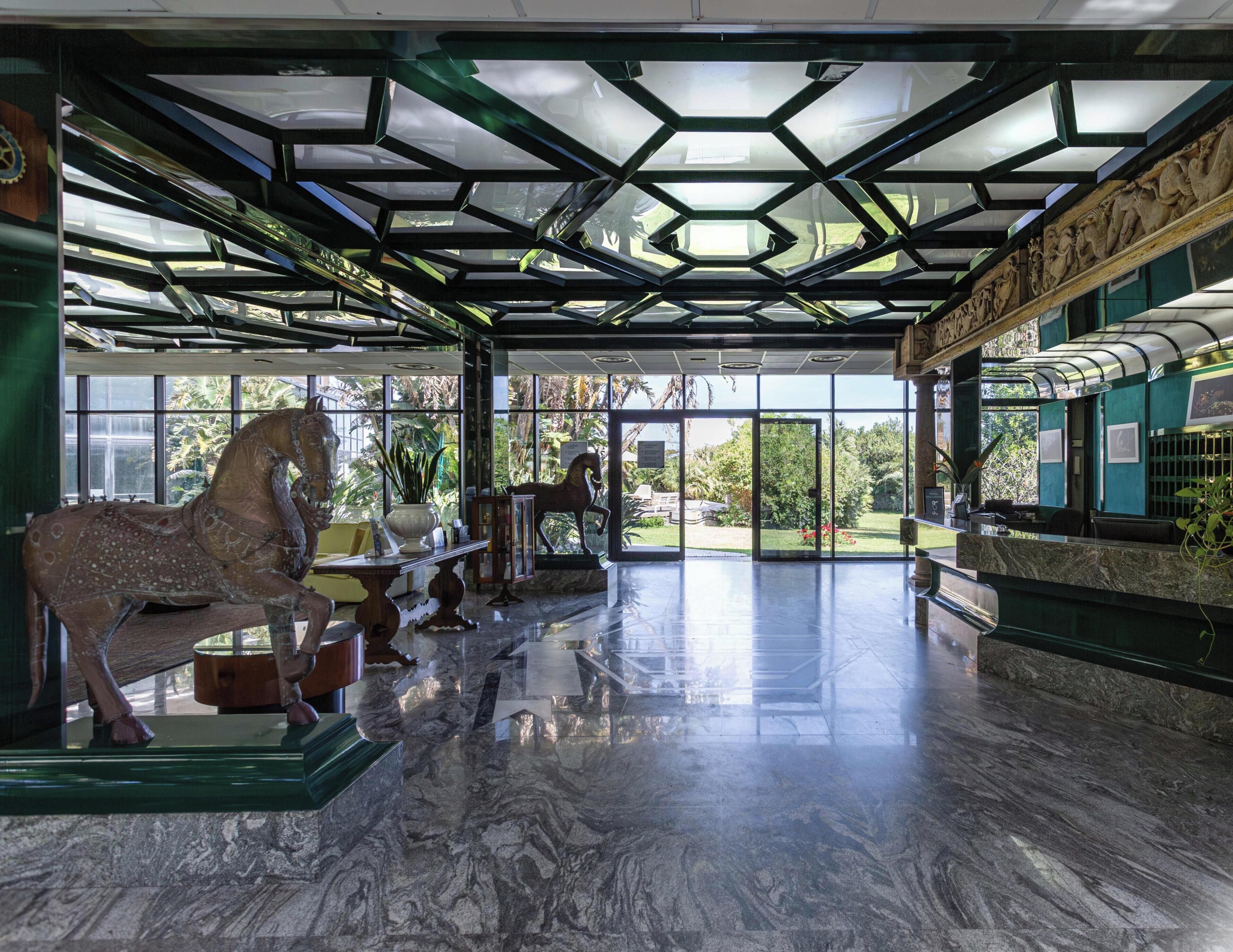 Eine großzügige Lobby mit Glasdecke, einer Pferdestatue und einem Empfangstresen.