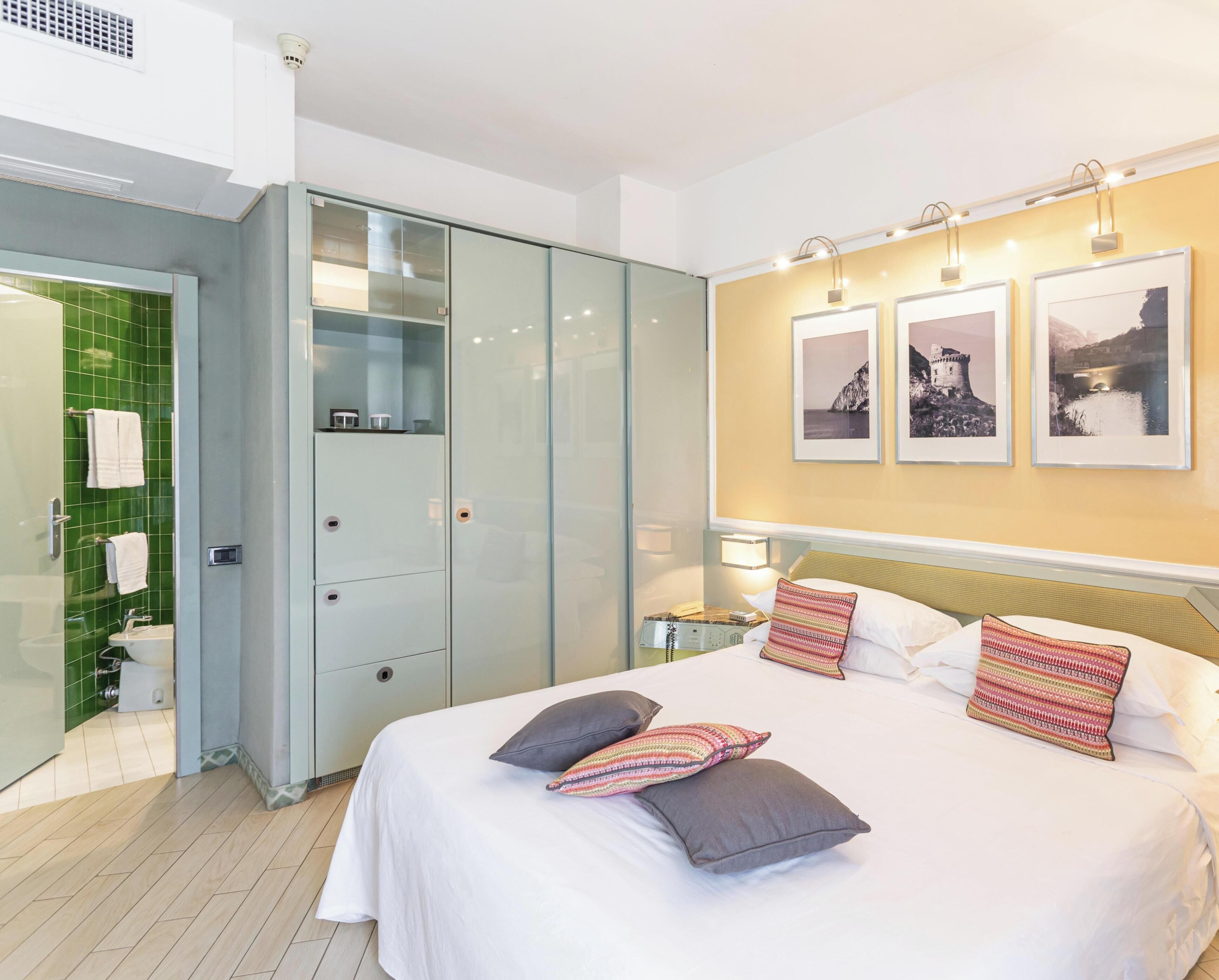 Una habitación de hotel con una cama, un armario, un baño y tres cuadros en la pared.