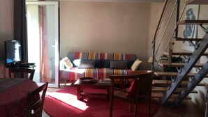 Un salon comprenant un canapé, un téléviseur, une table à manger avec des chaises et un escalier.