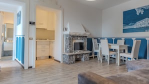 Una sala de estar moderna con chimenea, un comedor con sillas blancas y una cocina al fondo.