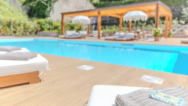 Un área junto a la piscina con una mesa de madera, una toalla blanca y una silla de descanso.