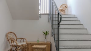 Una escalera con barandilla de metal, sillas de mimbre, un banco de madera y una planta en maceta.