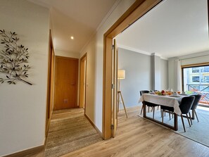 A hotel room with a dining area, wooden flooring, a lamp, and a view of the outside.