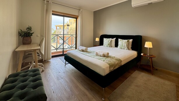 A bedroom with a bed, bedside tables, a desk, a chair, a potted plant, and a view through a balcony door. - ALBUFEIRA MODERN 7 WITH POOL by HOMING (Albufeira)