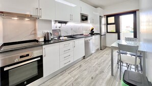 Eine moderne Küche mit weißen Schränken, einem Edelstahlbackofen, einer Mikrowelle und einem Kühlschrank. Ein Esstisch mit Stühlen und ein Fenster mit Blick sind ebenfalls vorhanden.
