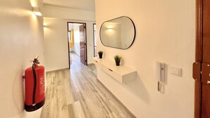 Ein Flur mit Feuerlöscher, einem Spiegel, einer Pflanze und einem Lichtschalter an der Wand.
