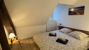 A bedroom with a sloped ceiling, a bed with patterned bedding, a bedside table with a lamp, and a painting on the wall.