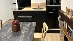 A compact kitchen with a black countertop, a sink, and a microwave above it. There is a chair and a table with a vase of flowers.