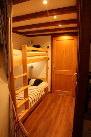 A room with bunk beds, a wooden door, and a small table with a lamp. - Apartment La Corniche, Central Morzine, sleeps 6 (Morzine)