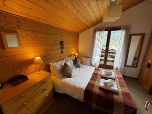 A wooden-paneled bedroom with a bed, bedside lamp, dresser, and a window with curtains.