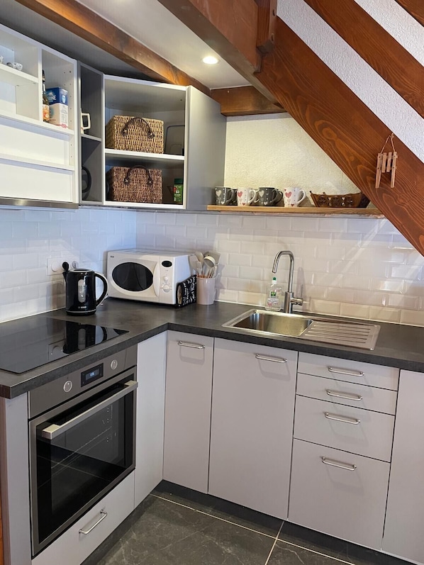 A modern kitchen with white cabinetry, a black countertop, a built-in microwave, a coffee maker, and a stainless steel sink. - Apartment La Corniche, Central Morzine, sleeps 6 (Morzine)