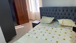 A bedroom with a large bed, two pillows, a nightstand, and a wooden door. - CHALWE HOTEL APART (Kigali)