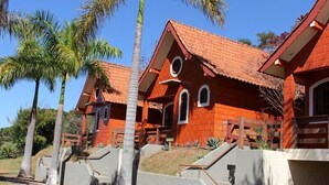Una hilera de cabañas de techo rojo con un diseño simétrico, rodeadas de palmeras y un cielo despejado.