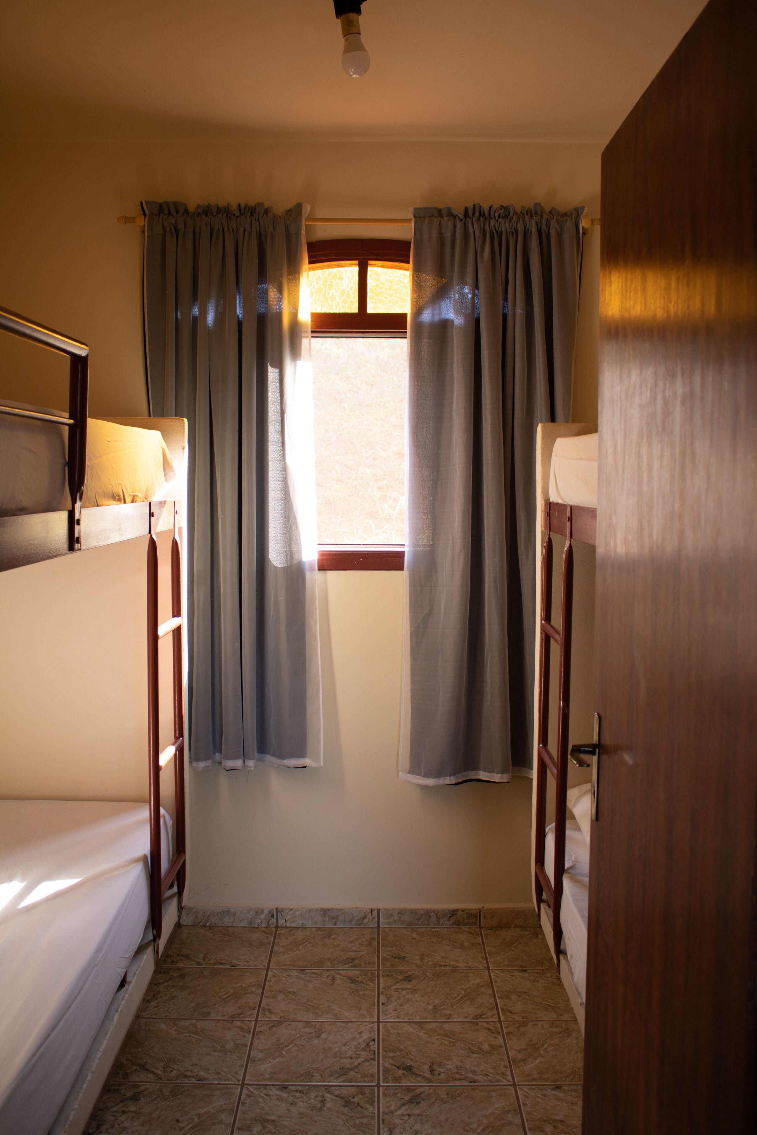 Una habitación con dos literas, una ventana con cortinas y suelo de baldosas.