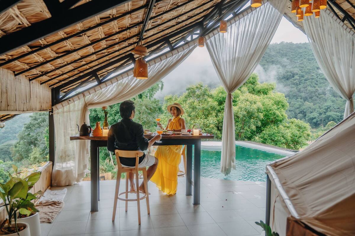 A dining area with a table and chairs, a view of a lush green landscape, and a pool.