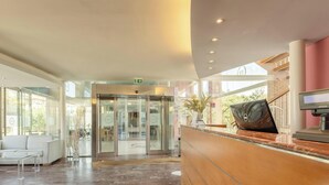 A hotel lobby with a reception desk, a glass elevator, and a seating area with a sofa and chairs. - Hotiday Room Collection - Calambrone (Calambrone)