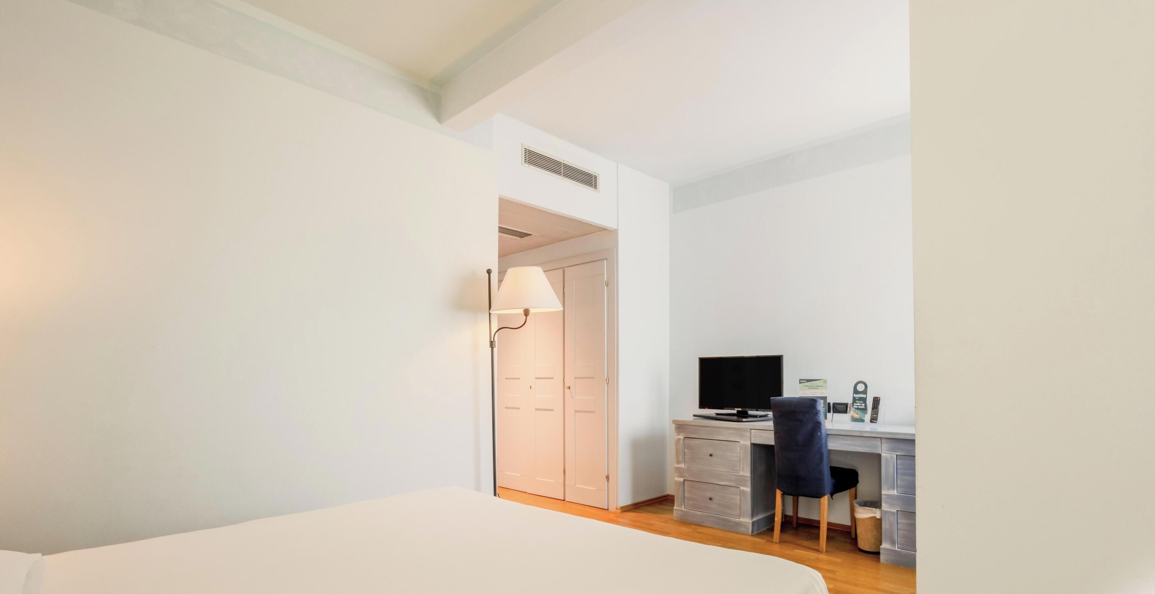 A hotel room with a bed, a desk with a computer, and a chair.