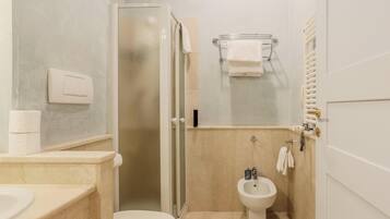 A compact bathroom with a toilet, bidet, and a glass-enclosed shower.