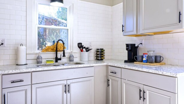 A kitchen with white cabinets, a window with a view, a sink with a faucet, and various kitchen items on the counter. - The Bluegrass Railway Inn (Midway)