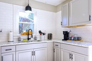 Une cuisine avec des meubles blancs, une fenêtre donnant sur un beau paysage, un évier avec un robinet et divers ustensiles de cuisine disposés sur le plan de travail.