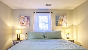 A bedroom with a bed, two bedside lamps, a window with a curtain, and two wall-mounted paintings. - The Bluegrass Railway Inn (Midway)