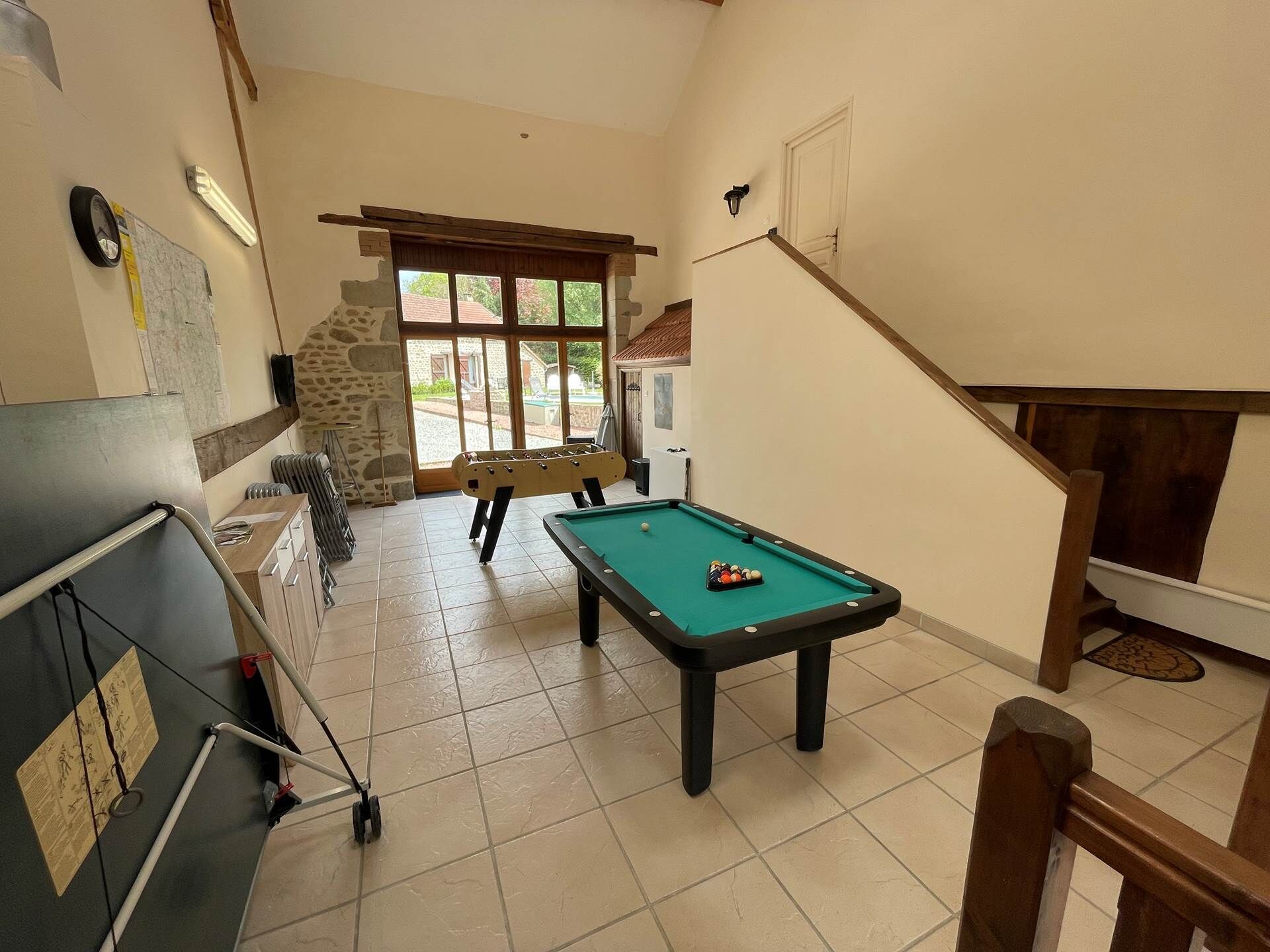 Una mesa de billar en una habitación con pared de piedra, una ventana y una escalera.