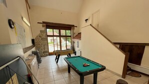 A pool table in a room with a stone wall, a window, and a staircase.